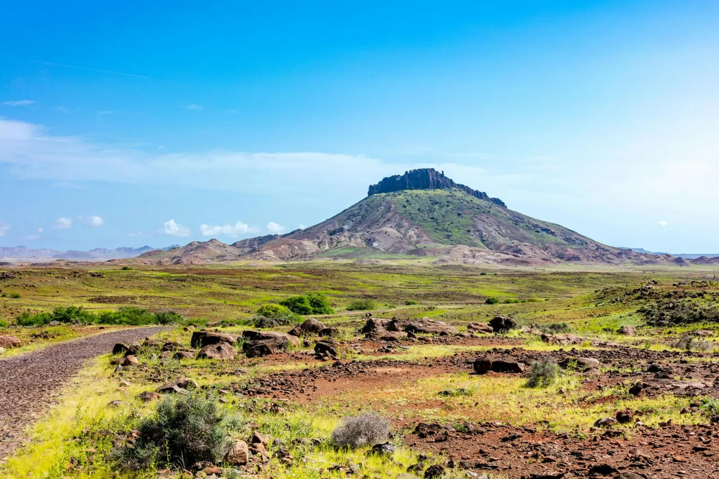 Piste de terre menant à un relief volcanique au milieu de la verdure